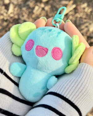 Close-up of a blue plush stuffed toy with pink circular patches, held in a striped sweater sleeve.