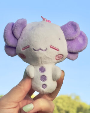 Small plush stuffed animal with purple ears held up against a clear blue sky.