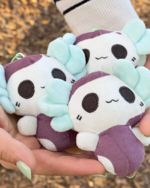 Close-up of a pastel purple and mint plush panda being held in a person's hands outdoors, showing cute facial features and soft fabric.