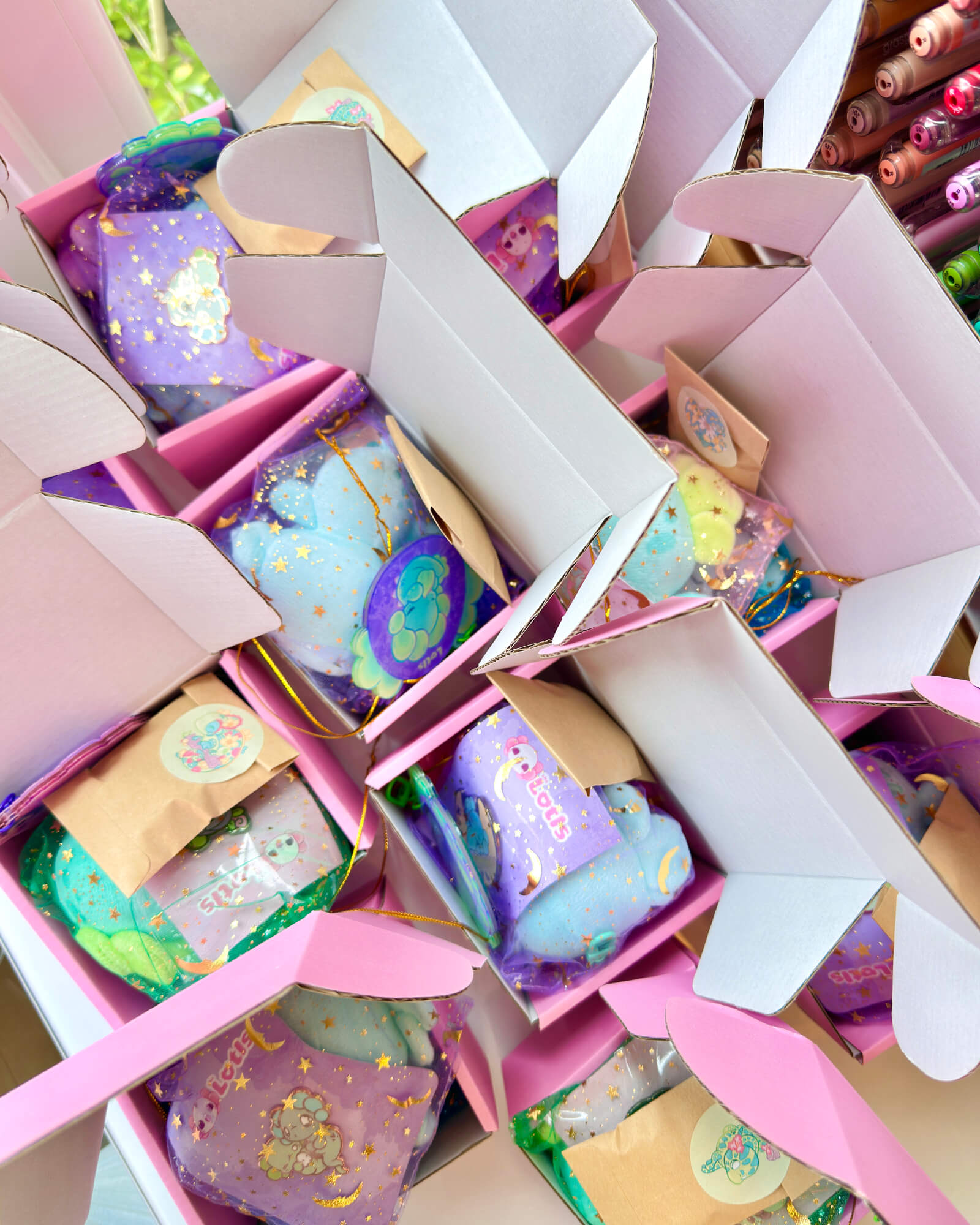 Mini Lotl Box Mystery B Grades by Evy Benita 3 - Evy Benita Close-up of pastel pink and purple gift boxes filled with colorful wrapped favors, accented with gold stars and ribbons.