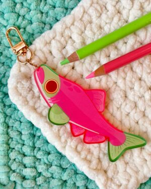 Close-up of green and pink pencils attached to a pink bird-shaped keychain on a fluffy blue and white rug.