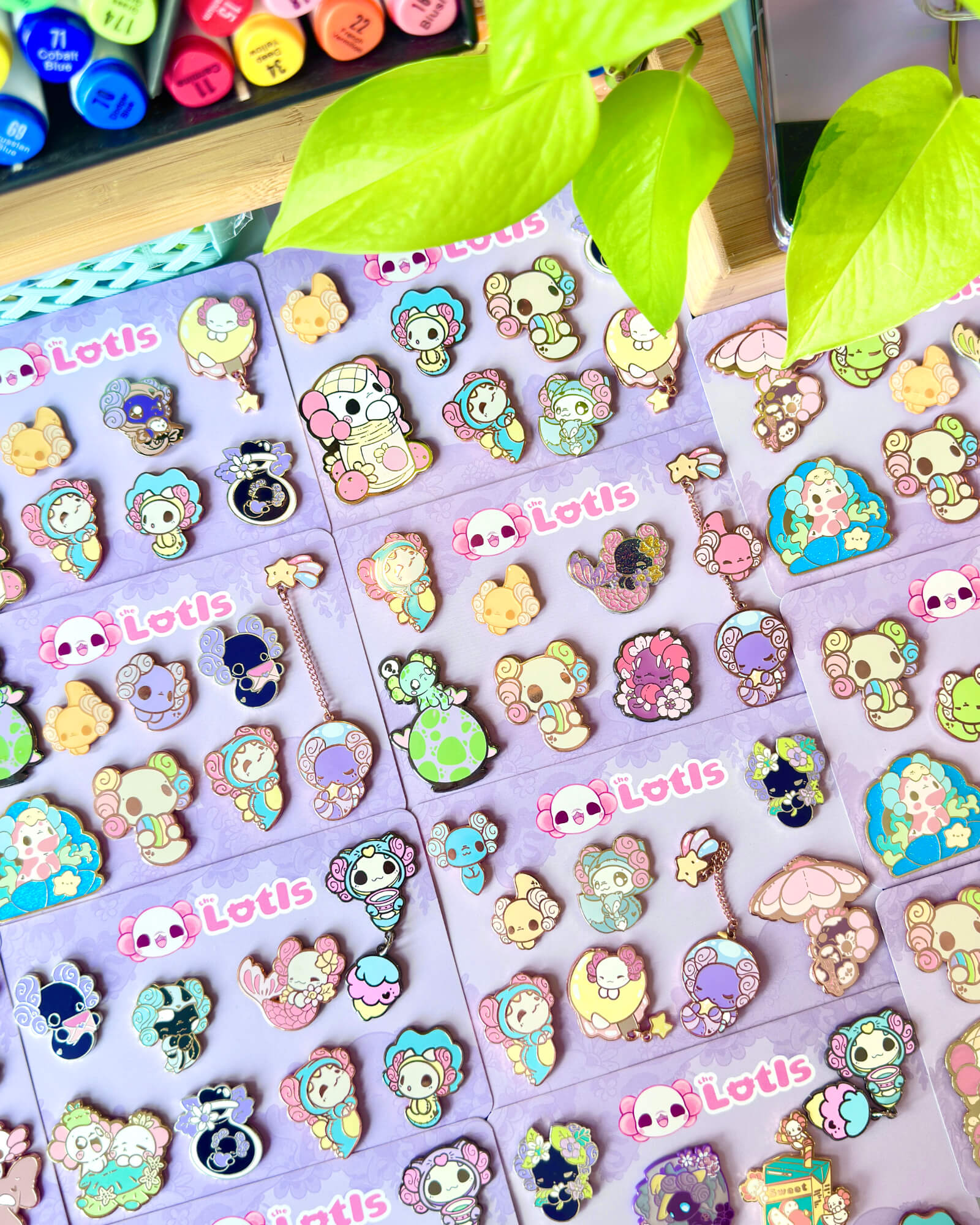 The Lotls B Grade Mystery Enamel Pin Sets 2 - Evy Benita Assorted colorful cartoon pins and keychains laid out on purple display cards labeled 'Lotis'