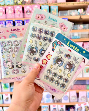 The Lotls Mystery Sticker B Grade Grab Bags 2 - Evy Benita Person holds several shiny sticker sheets with colorful cartoon animals in a store aisle.