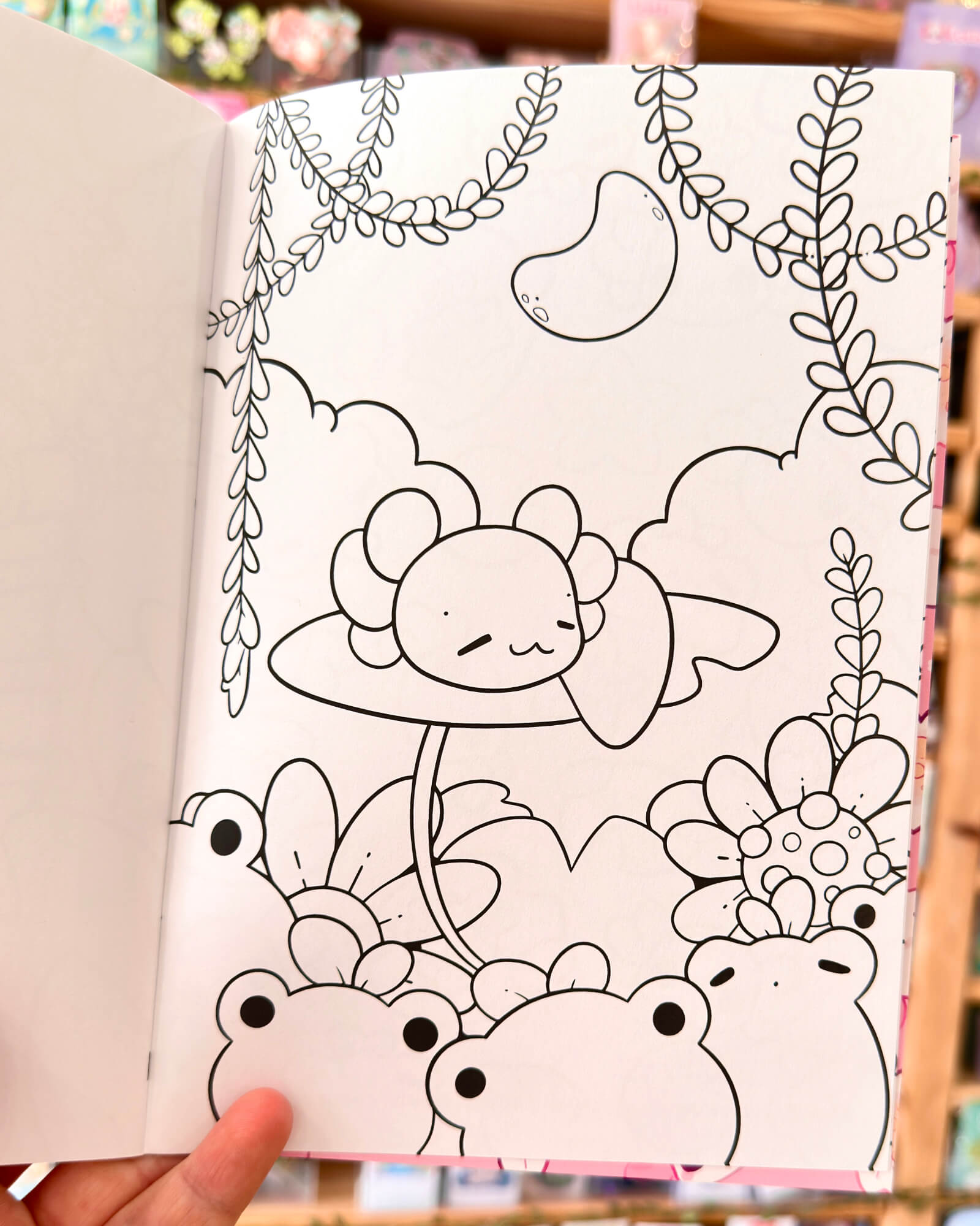 The Lotls in Lily Pond Valley Coloring Book 1 - Evy Benita Black-and-white coloring page with a cute sleepy bear resting on a platform, surrounded by flowers and hanging vines.