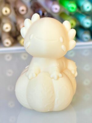 Close-up of a pale white dinosaur toy with rounded body and small dorsal spikes, photographed against a colorful blurred background.
