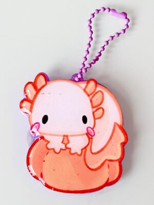 Cartoon pig keychain in pink and orange with a purple bead chain against a light background.