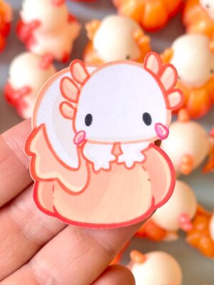 Close-up of a pink cartoon chick cutout held between fingers, with an orange, out-of-focus background.