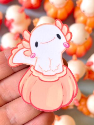 Close-up of a pink cartoon turkey cutout being held between fingers, smiling face, with orange shapes blurred in the background.
