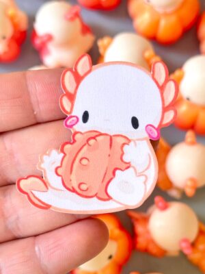 Close-up of a pink cartoon chicken charm being held between fingers, with orange and cream bead accents in the background
