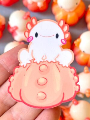 Close-up of a pink cute jellyfish-shaped charm being held between fingers, with a soft smile and orange-accented edges.